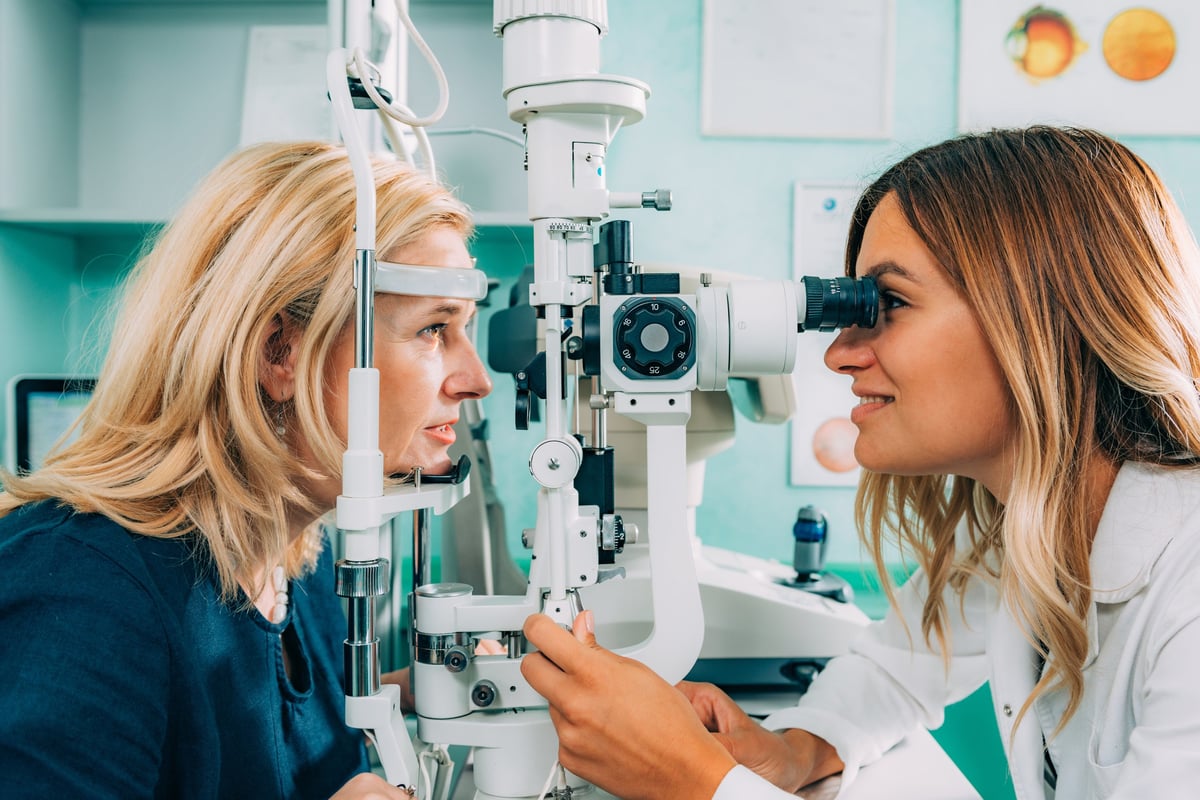 Un optometrista examina los ojos de un paciente con una lámpara de hendidura en un entorno clínico.